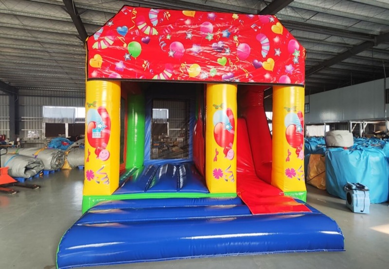 Red bouncy castle with balloon and confetti design and slide for parties in Cork
